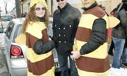 Drei Menschen in Bienenkostümen, zwei Frauen und ein Mann, stehen im Winter draußen mit Autos und Schnee im Hintergrund.