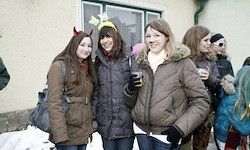 Vier Frauen stehen draußen in Winterkleidung. Sie lächeln und scheinen für ein Foto zu posieren. Eine Frau trägt eine Weihnachtskopfbedeckung.