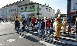 Eine Gruppe von Menschen in Kostümen überquert eine Straße vor Gebäuden mit Geschäften und Schildern.