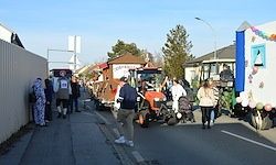 Eine Parade mit Traktoren und Menschen, die auf der Straße gehen, einige mit Luftballons. Die Traktoren sind mit bunten Luftballons verziert.