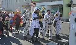 Eine Parade von Menschen in Kostümen, einschließlich einer Person in einem Dalmatinerkostüm, geht die Straße entlang.