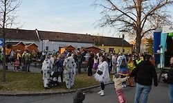 Eine große Gruppe von Menschen in verschiedenen Kostümen versammelt sich vor einem Gebäude, einige halten Kinder und andere gehen umher.