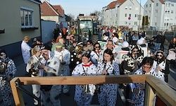 Eine Parade mit Menschen in Tupfenkostümen, die Musikinstrumente wie Trompeten und Posaunen spielen, auf einer von Gebäuden gesäumten Straße.