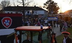 Ein Traktor ist auf einer Straße geparkt, in der Nähe steht eine Menschenmenge, ein Schild mit der Aufschrift 'ENTRADA' ist sichtbar. Ein Mann mit Hut steht vor dem Traktor.