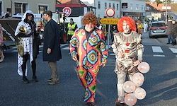 Eine Gruppe von Menschen in Clown-Kostümen, die auf der Straße gehen. Sie tragen Ballons und stehen in der Nähe eines Zebrastreifens.