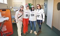 Vier Frauen stehen in einem Flur in Winterkleidung und nummerierten Startnummern. Sie lächeln für ein Foto. Dahinter befindet sich ein Schild mit dem Wort Städte und einem QR-Code.
