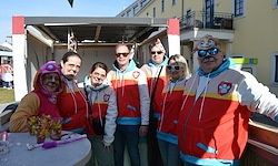Eine Gruppe von Menschen in passenden Jacken und Sonnenbrillen steht zusammen vor einem Gebäude. Sie posieren für ein Foto.
