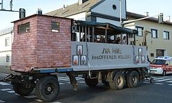 Ein Lastwagen mit einer Ziegelstruktur oben und den Worten JVA Halle fährt mit einem roten Krankenwagen dahinter die Straße entlang.