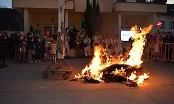 Eine Menschenmenge beobachtet ein großes Feuer auf der Straße, mit einer Metallkonstruktion und Menschen, die in der Nähe stehen.