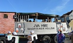 Ein Lkw mit einem Banner, auf dem JVA HME Besoffener Vollzug steht. Mehrere Menschen in weißen Hüten stehen vor dem Lkw.