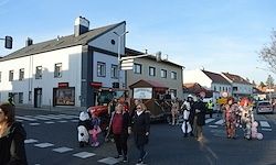 Menschen in Kostümen gehen vor Gebäuden über die Straße. Ein Lastwagen ist geparkt. Autos sind auf der Straße geparkt.