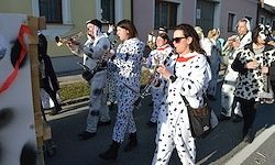 Eine Blaskapelle in Dalmatiner-Kostümen spielt auf der Straße und führt Posaunen, Tuben und Trompeten vor einem Gebäude auf.