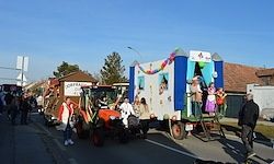Eine Straßenparade mit Traktoren, die mit Luftballons dekoriert sind, und Kindern, die darauf stehen, ein paar Leute gehen auf der Straße und einige Gebäude sind auf der rechten Seite.