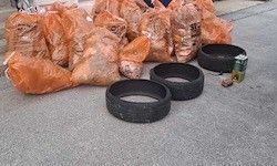 Orange Müllsäcke, zwei schwarze Reifen und eine Dose liegen auf einem Betonboden. Die Müllsäcke sind voll.