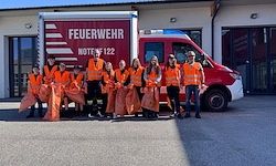 Eine Gruppe von Menschen in orangenen Westen posiert für ein Foto vor einem roten Feuerwehrwagen.