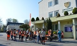 Eine Gruppe von Menschen in orange Westen steht vor dem Amthaus Schonador. Im Hintergrund sind Bäume und Gebäude zu sehen.