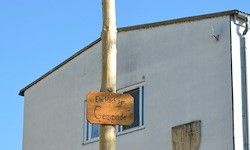 Ein Gebäude mit blauem Himmel im Hintergrund. Ein Schild mit den Texten 'Birkenhof' und 'Geschader' ist an einem Pfosten vor dem Gebäude montiert.