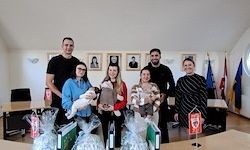 Eine Gruppe von Menschen in einem Raum mit Flaggen im Hintergrund. Sie halten Babys und stehen neben einem Tisch mit Geschenken.