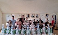 Eine Gruppe Erwachsener und Kinder posiert für ein Foto in einem Raum mit gerahmten Porträts, Flaggen und dekorierten Babygeschenkkörben.