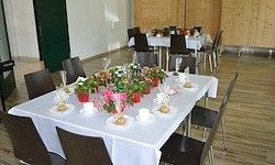 Ein Esszimmer ist mit Blumen, Tellern und Tassen eingerichtet. Der Raum hat Holzböden und weiße Wände, mit schwarzen Stühlen um einen langen Tisch, der mit Weiß bedeckt ist.