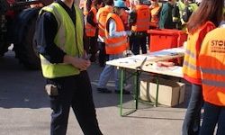 Eine Gruppe von Menschen in Warnwesten steht um einen Tisch mit Gegenständen darauf, einer von ihnen hält ein Werkzeug.