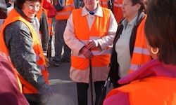 Eine Gruppe von Frauen in orangefarbenen Sicherheitswesten steht draußen, lächelt und unterhält sich. Eine Frau hält einen Gehstock.