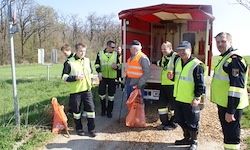Eine Gruppe von Personen in Sicherheitswesten, einschließlich eines Mannes mit weißem Bart, steht vor einem roten Lastwagen an einem sonnigen Tag.
