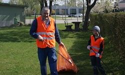 Ein Mann und ein Kind in orange Sicherheitswesten reinigen mit Müllsäcken das Gras in einem Vorstadtpark.