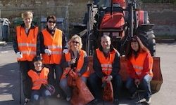 Eine Gruppe von Menschen in orangenen Westen und Handschuhen posiert für ein Foto mit einem Traktor und Müllsäcken im Hintergrund.