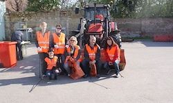 Eine Gruppe von Menschen in orangenen Westen posiert vor einem roten Traktor und einem roten Mülleimer.
