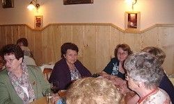 Eine Gruppe älterer Frauen sitzt in einem gemütlichen Restaurant mit Holzwänden und Bilderrahmen um einen Tisch herum.