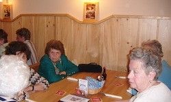 Eine Gruppe älterer Frauen sitzt in einem Restaurant mit Holzwänden und gerahmten Bildern an einem Holztisch.