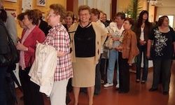 Eine Gruppe von Frauen steht in einem Flur, einige mit Brille und Jacken. Sie scheinen miteinander zu sprechen.