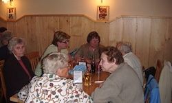 Eine Gruppe älterer Frauen sitzt in einem Restaurant um einen Tisch herum, plaudert und genießt Getränke. Die Holzwände und die gedämpfte Beleuchtung schaffen eine gemütliche Atmosphäre.