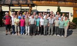 Eine Gruppe von Menschen, die verschiedene Kleidungsstücke und Schuhe tragen, posiert für ein Foto vor einem Gebäude mit Balkon und Pflanzen.