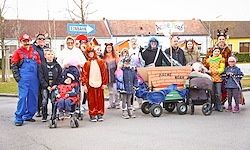 Eine Gruppe von Menschen in Kostümen posiert für ein Foto auf der Straße mit mehreren Kinderwagen und einem Schild.