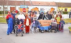 Eine Gruppe von Menschen in Kostümen, die Kinderwagen und Karren schieben, posiert für ein Foto in einem Dorf.