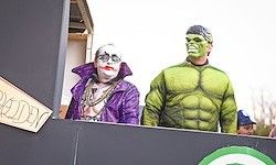 Zwei Menschen in Kostümen, einer in einem lila Outfit und der andere in einem grünen Hulk-Kostüm, stehen auf einer Bühne mit Hintergrund.