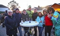 Eine Gruppe von Menschen in Winterkleidung steht um einen Tisch mit Flaschen herum und posiert für ein Foto im Freien. Ein Mann in einem Hulk-Kostüm steht unter ihnen.