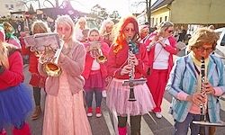Eine Gruppe von Menschen in rosa und roten Kostümen spielt auf der Straße Musikinstrumente.