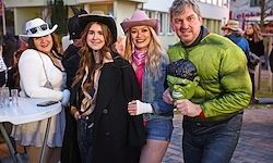 Vier Menschen in Kostümen posieren für ein Foto im Freien vor einem Tisch und Gebäuden im Hintergrund.