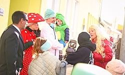Eine Gruppe von Menschen in Kostümen steht draußen auf einer Straße, wahrscheinlich für eine Halloween-Veranstaltung, mit einem Mann in Anzug und einer Frau in einem roten Mantel.