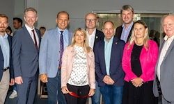 Eine Gruppe von formell gekleideten Männern und Frauen steht zusammen in einem Raum. Sie lächeln für ein Foto.