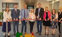 Eine Gruppe formell gekleideter Personen steht in einer Reihe, hält ein Band und posiert für ein Foto in einem Büroflur.