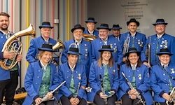 Eine Gruppe von Musikern in blauen Uniformen und Hüten, einschließlich Tuba-, Trompeten- und Flötenspielern, posiert für ein Foto.