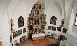 Ein Blick von oben auf eine Kapelle mit Altar, kunstvollen Verzierungen, gerahmten Bildern, einem Teppich, Stühlen und einem Tisch.