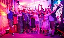 Eine Gruppe von Menschen in traditioneller Kleidung steht zusammen, hebt die Hände und lächelt, wahrscheinlich bei einem Festival.