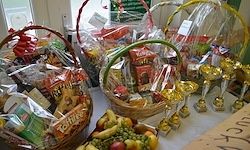 Ein Tisch voller verschiedener Körbe mit unterschiedlichen Artikeln, einschließlich Obst, Snacks und Geschenkartikeln. Einige Körbe haben Plastikabdeckungen. Im Hintergrund ist ein Fenster zu sehen.