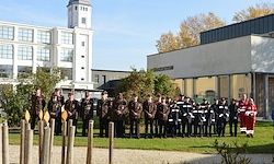 Eine Gruppe von Menschen in Uniform steht vor einem Gebäude. Eine Person in einem roten Outfit steht auf der rechten Seite.