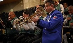 Ein Mann in einem blauen Anzug spielt Trompete, während er neben anderen Musikern, die Trompeten halten, in einem Konzertsaal sitzt.